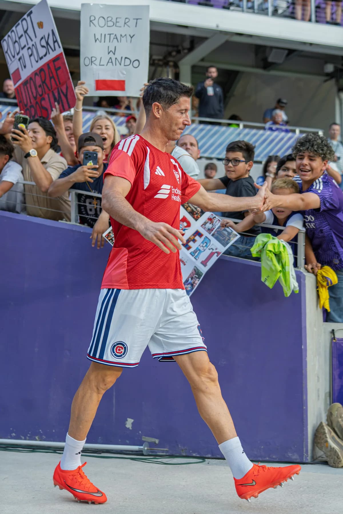A player in a red training shirt greeting fans holding signs at the stadium