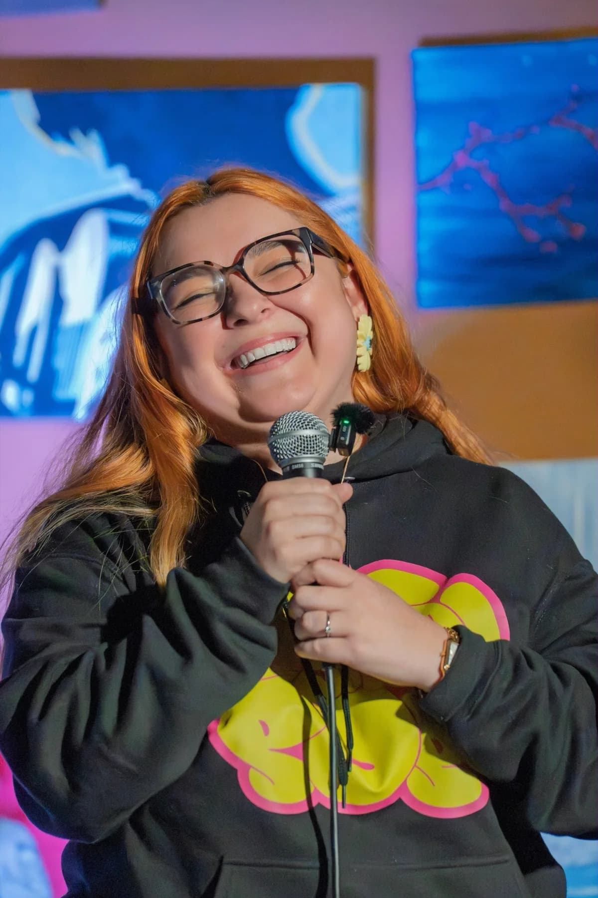 A smiling performer holding a microphone in front of framed artwork