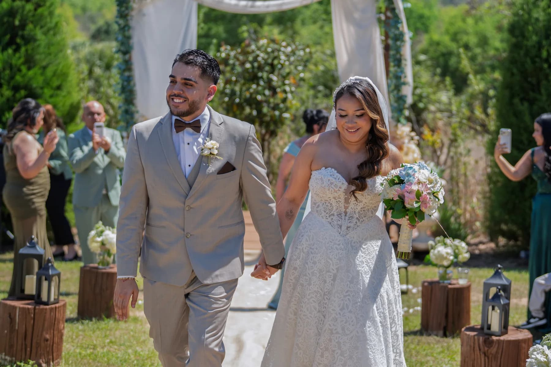 A wedding couple walking past a floral arch as guests applaud outdoors